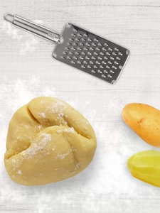 A view from above of baking dough, potatoes and a grater. 