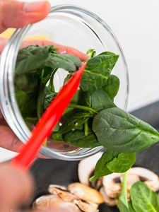 A hand scoops spinach leaves out of a glass bowl.