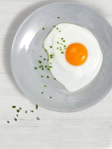 A grey plate with a perfectly fried egg and a dusting of herbs.