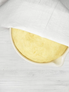 Yeast dough resting in a ceramic bowl and partially covered with a napkin.