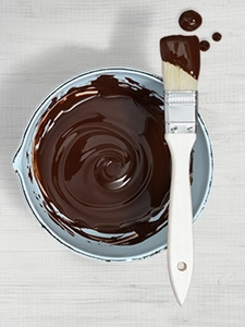 A jug of melted chocolate with a brush resting on top and few drips of chocolate on the counter.