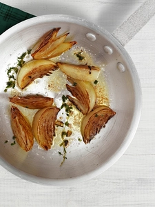 Perfectly crispy onion quarters spaced out in a pan with herbs.