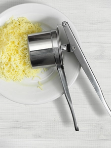 A ricer rests on a plate next to perfectly pureed potato squiggles.