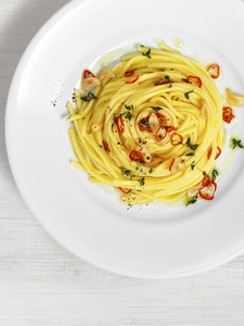 A mound of pasta on a plate sprinkled with chilli and herbs.