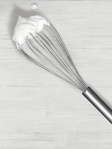 A steel whisk with a whipped cream peak at its tip.