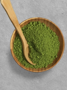 A bowl of green matcha powder with a wooden spoon in it.