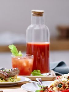 Freshly squeezed fruit juice in bottle next to dishes made with food mincer including sausages, salads and falafel.