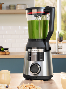 Un frullatore Bosch con una ciotola di smoothie verde, su un tavolo di legno, in una cucina moderna e luminosa.