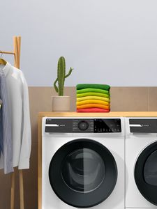 wasmachine en droger naast elkaar met stapeltje kleding en cactus bovenop