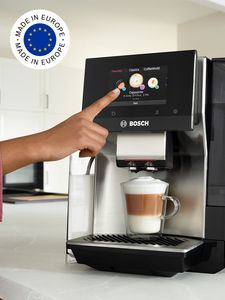 VeroCafe machine on kitchen top featuring a cup of cappuccino and European flag in image top corner.