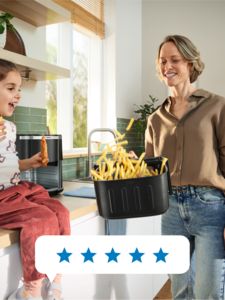 Uma mãe abana o cesto de uma Air Fryer da Bosch enquanto a sua filha se senta no balcão da cozinha, sorrindo e apreciando o processo de confeção em conjunto.