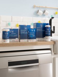 Uma bancada com vários produtos de limpeza para máquinas de lavar loiça da Bosch junto a uma máquina de lavar loiça em aço inoxidável numa cozinha luminosa.