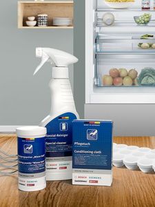 Imagem apresenta produtos de limpeza para frigoríficos: um spray, um em pó, pano de limpeza, sobre uma superfície de madeira. 