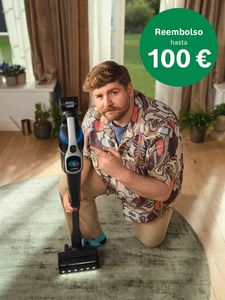Hombre de rodillas, señalando una aspiradora moderna en el suelo. Un círculo verde indica un reembolso de hasta 100 €.