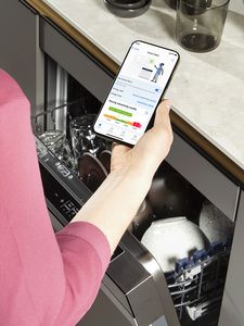 Frau steht mit Home Connect App vor geöffnetem Bosch Geschirrspüler