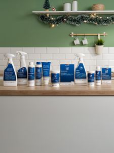 Uma variedade de produtos de limpeza exibidos  numa bancada de madeira com uma parede verde, com decorações para o natal.