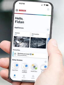 Telefon tutan və ekranına diqqətlə baxan bir kişi. Home Connect tətbiqi və əsas ekran g&ouml;r&uuml;n&uuml;r.