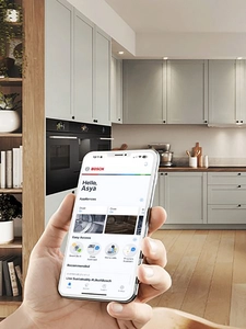 Bir insan telefonu incə şəkildə tutur, diqqəti Home Connect əsas ekranına y&ouml;nəlib, arxa planda isə isti, rahat bir mətbəx g&ouml;r&uuml;n&uuml;r.