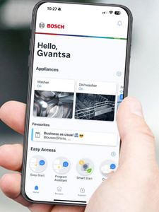 მამაკაცი უჭირავს ტელეფონი და ფოკუსირებულია მის ეკრანზე. ჩვენ ვხედავთ Home Connect აპლიკაციას და მთავარ ეკრანს.       