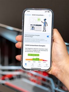 Eine Hand h&auml;lt ein Smartphone mit einer App, die den erwarteten Anteil erneuerbarer Energie an der Stromlast f&uuml;r die kommenden 24 Stunden anzeigt.