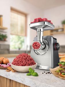 Bosch Fleischwolf in moderner K&uuml;che, verarbeitet frisches Fleisch, Hackfleisch in Sch&uuml;ssel, Zutaten und Burger daneben.