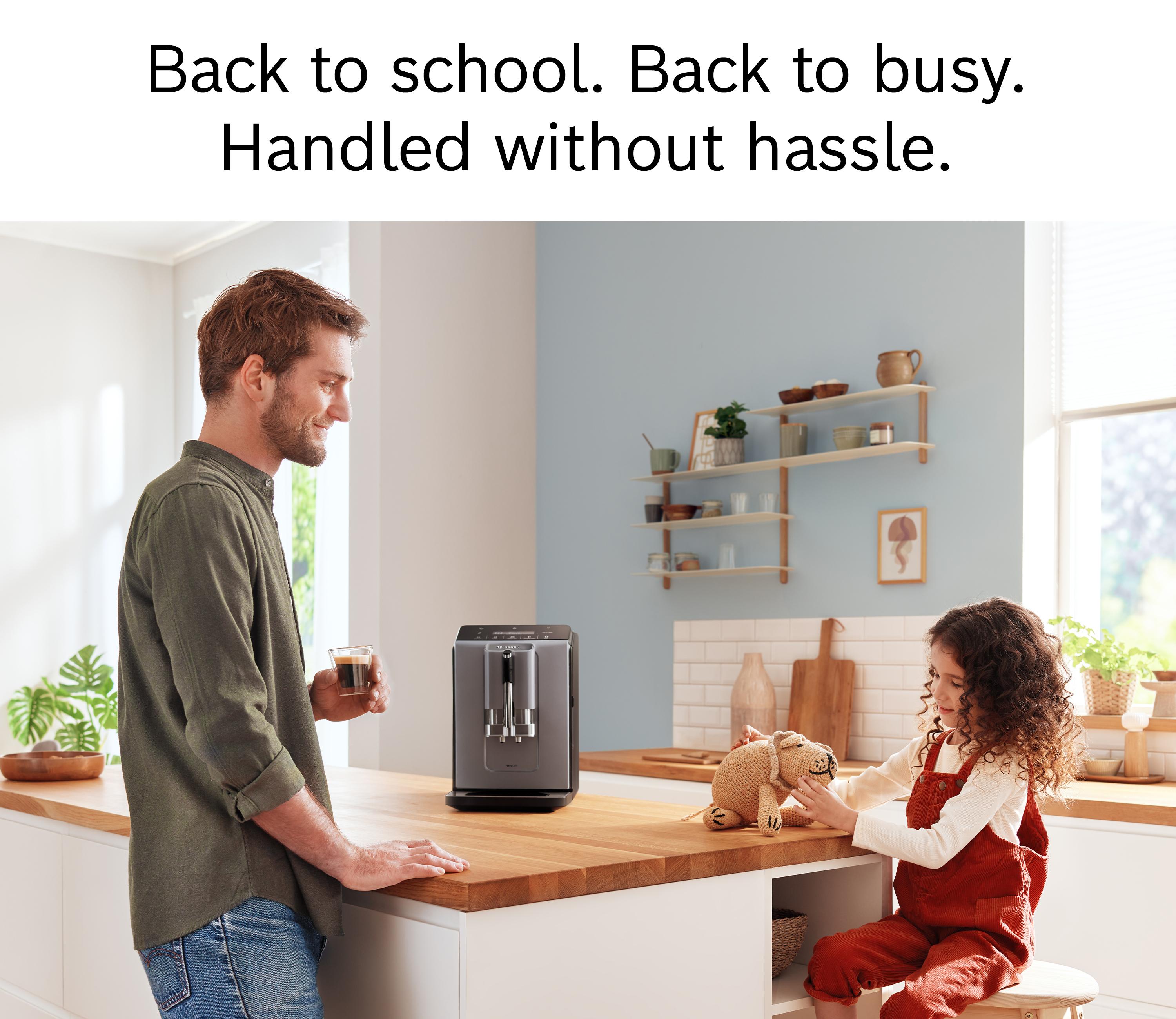 Man with coffee by a Bosch coffee machine on a kitchen counter, child playing nearby.