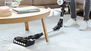 A person vacuuming under a table with an Unlimited vacuum cleaner
