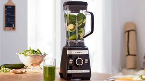 Bosch Blender VitaBoost with fruits and vegetables and a smoothie glas on a kitchen shelf.