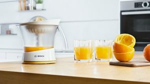 Цитрус преса VitaPress на Bosch с портокалов сок върху кухненски плот.