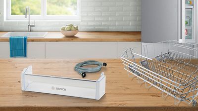 Diferentes peças de reposição Bosch sobre uma bancada de madeira de uma cozinha branca.