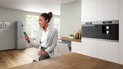 Woman sitting in the kitchen holding a smartphone in her hand.