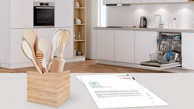 Diferentes productos de limpieza y mantenimiento Bosch y documentos sobre una mesa blanca en una cocina abierta.