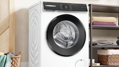 Lavatrice Bosch a carica frontale in una lavanderia domestica, accanto a scaffali con asciugamani e cesti in vimini