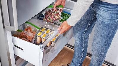 Persona che apre il cassetto del congelatore e sistema sacchetti di alimenti congelati