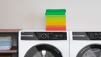 Lavatrice Bosch a carica frontale con sopra una pila di asciugamani piegati, colorati dal verde al rosso