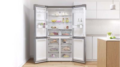 Un moderno frigorifero a quattro porte aperto in una cucina luminosa, mostrando scaffali organizzati con cibo e bevande all'interno.