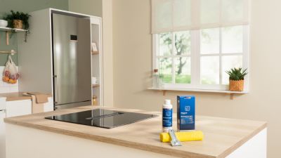 Piano cottura a induzione Bosch su un'isola da cucina con prodotti Cleaning&Care e panno in microfibra per la pulizia
