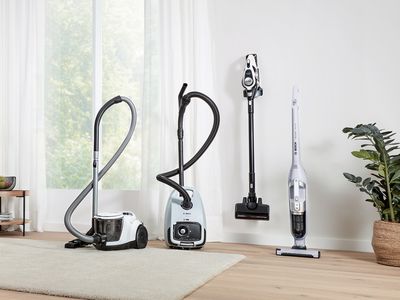 A lineup of four different vacuum cleaners in a bright hallway.