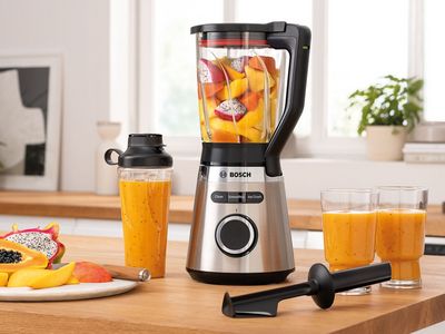 Een VitaPower Serie 4 blender gevuld met fruit, enkele smoothieglazen en een ToGo-fles op een keukenplank.