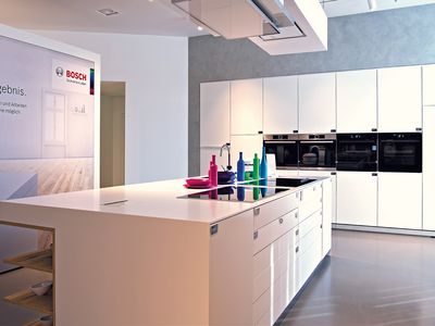 Weiß strahlende Küche mit Kochinsel und Aufsteller mit Schriftzug Einfach zum perfekten Ergebnis.