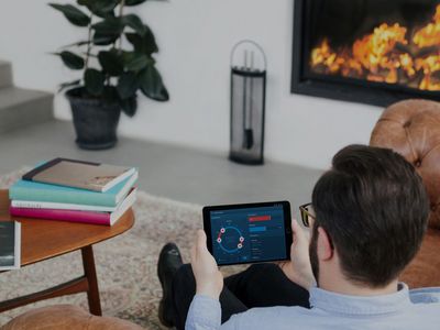 Ein Mann sitzt auf einem Sofa mit einem Tablet in der Hand auf dem die Smart Home App geöffnet ist.