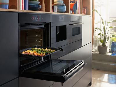 Open oven in a modern kitchen with vegetables on the baking tray.