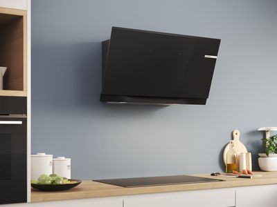 An inclined cooker hood is mounted on a blue-grey wall above a hob in a modern kitchen.