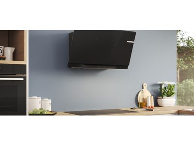 An inclined cooker hood is mounted on a blue-grey wall above a hob in a modern kitchen. 
