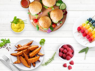 Eine Reihe gesunder Lebensmittel, u. a. Obstspieße und Süßkartoffelecken, auf einer weißen Arbeitsplatte.