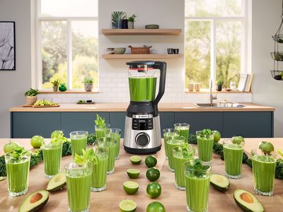 Der VitaPower Serie 6 steht inmitten vieler Gläser mit grünen Smoothies, Avocados und Limetten, die alle strahlenförmig um das Gerät auf der Arbeitsplatte in der Küchen angeordnet sind.