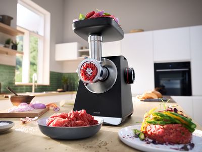 MultiPower Serie 6 cu dispozitivul de mărunţire şi carne &icirc;n tavă, pe un blat din bucătărie, alături de o farfurie cu bucăţi de carne.