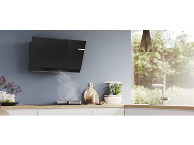Mūsdienīga virtuve ar elegantu melnu ventilatoru, tvaiku, kas paceļas no pannas, un koka darba virsmu.