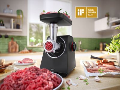 MultiPower serije 4 s nastavkom za mljevenje mesa i tanjurom s mljevenim mesom pored tanjura s kobasicama na kuhinjskom pultu.