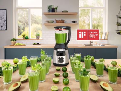 Een VitaPower Serie 6 op een keukentafel, omringd door enkele glazen met groene smoothies, avocado's en limoenen.